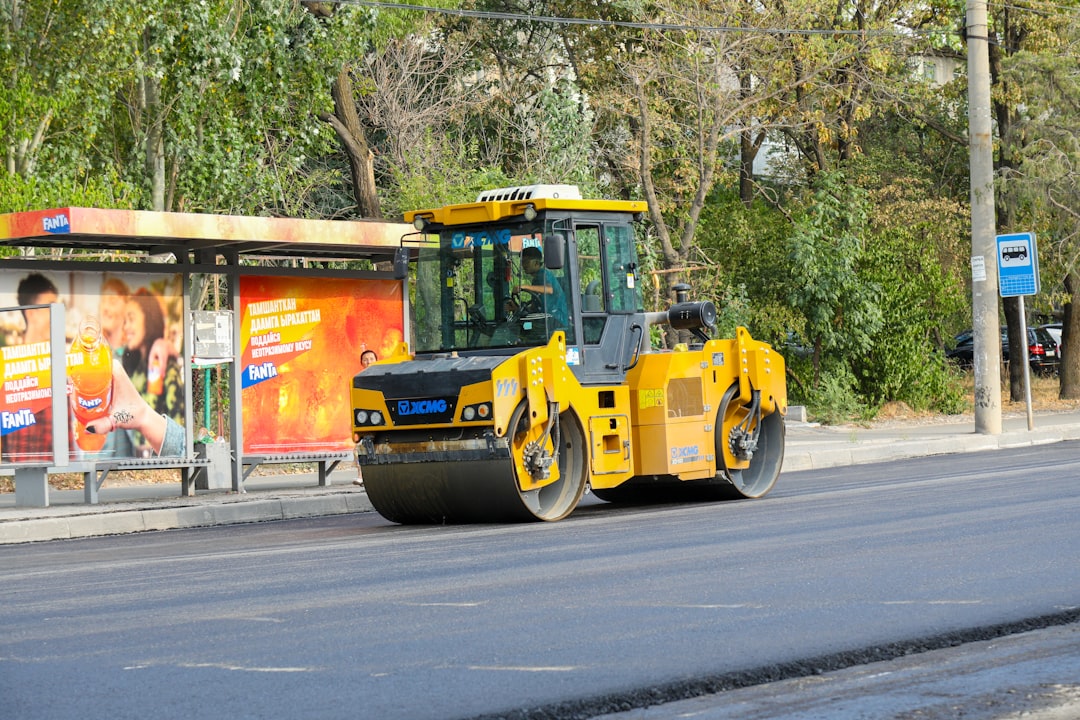 A road roller machine smoothing a new asphalt layer during road construction, with a focus on the machinery and street environment