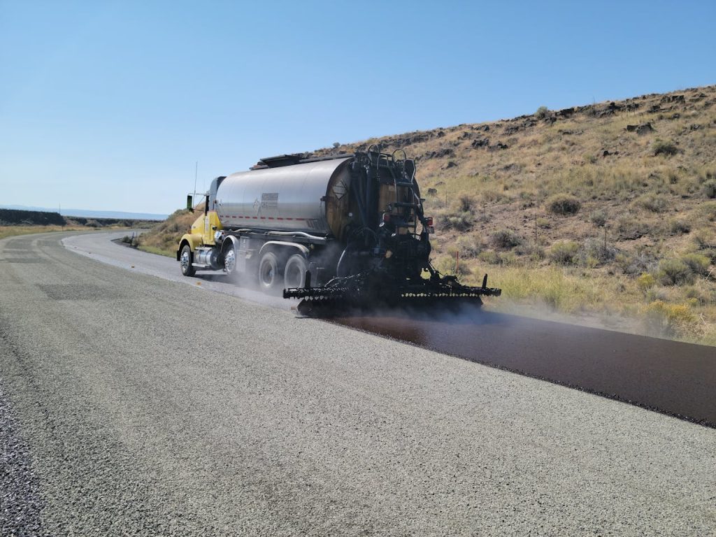 A road tanker applying asphalt on a rural road in Oregon under clear skies.