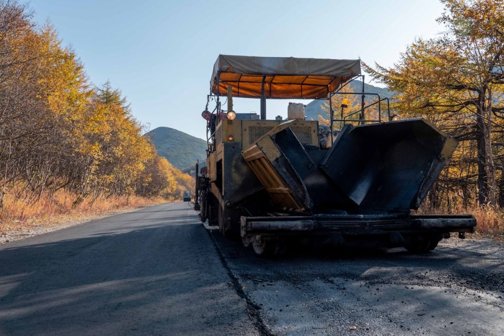 Road paving machine on a scenic autumn highway surrounded by colorful trees.