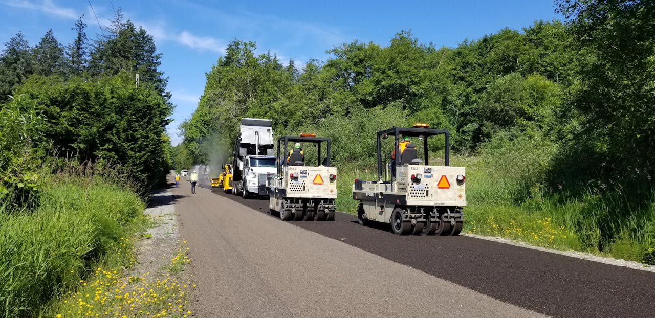 Asphalt road construction with pneumatic tire rollers in a forest area of Washington.